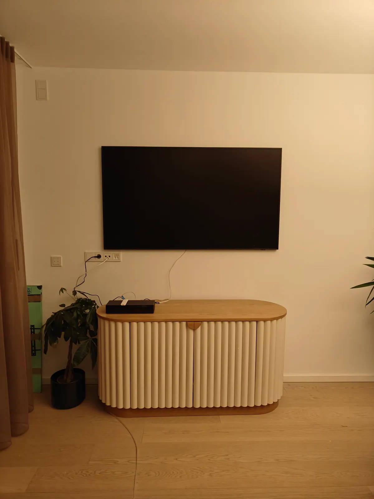 Schwarzer Wandfernseher über hellem Sideboard