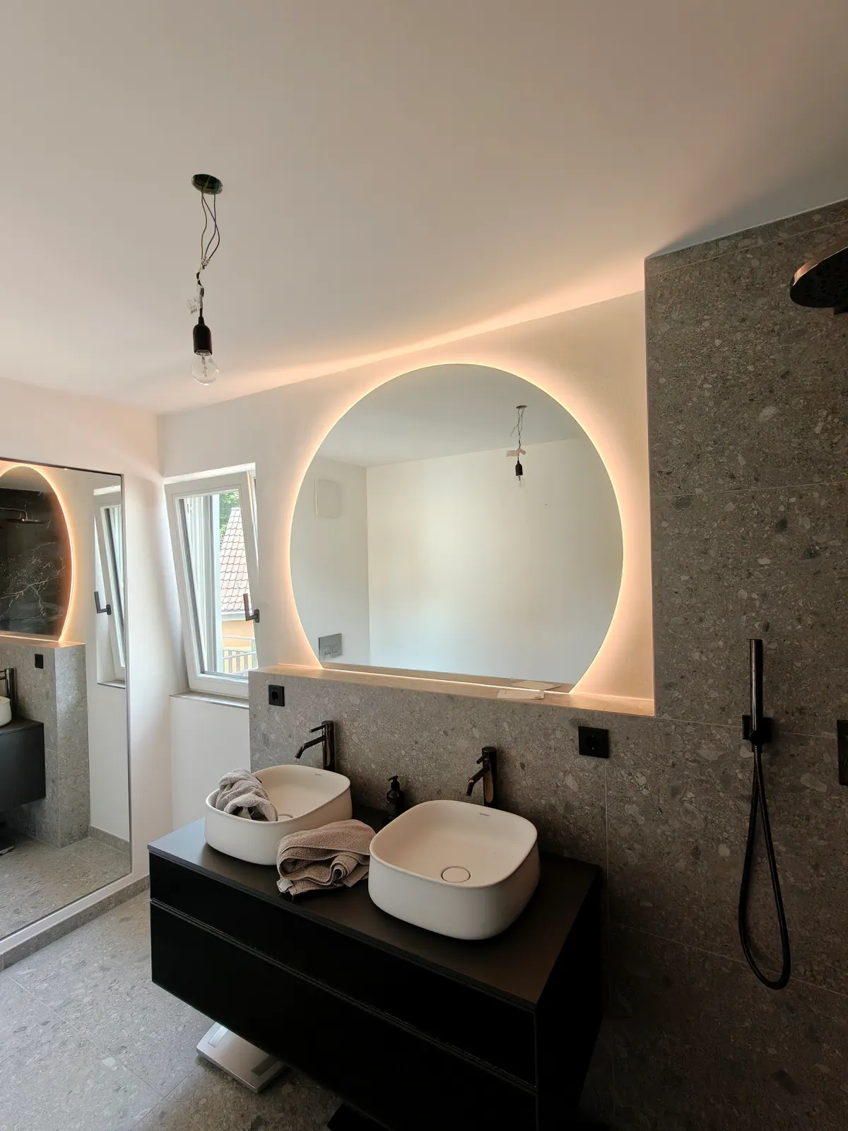 Badezimmer mit schwarzem Waschtisch und rundem hinterleuchtetem Spiegel